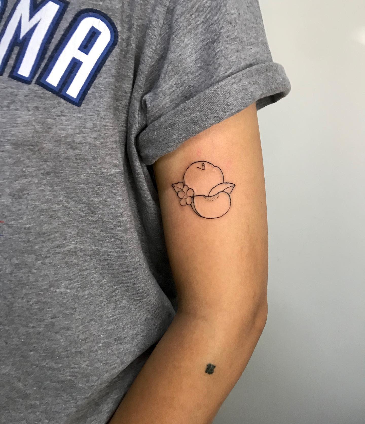Minimalist linework tattoo of a whole peach with a slice and a small flower on the arm
